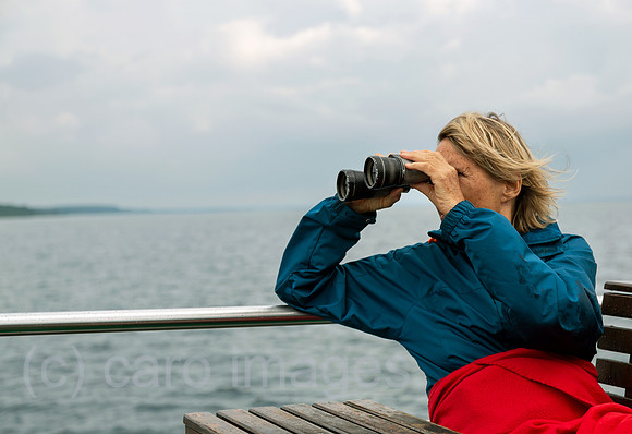 Deutschland, Waren (Mueritz) - Rentnerin schaut durch Fernglas auf Ausflugsdampfer auf der Mueritz, dem groessten See Deutschlands
