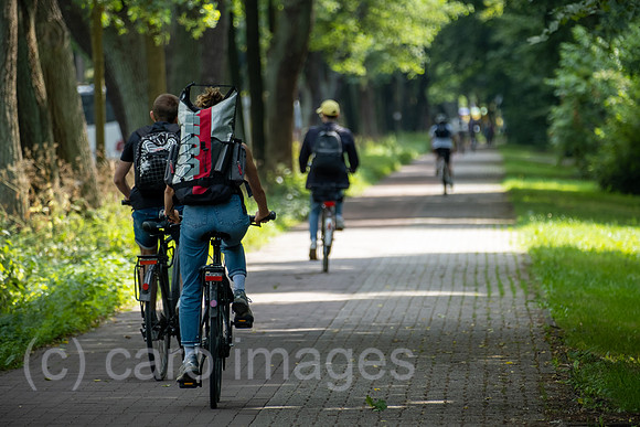 Deutschland, Bremen - Fahrradweg mit Fahrradfahrern an einer Strasse, rechts ein Park