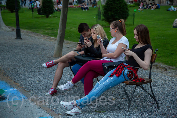 Kroatien, Zagreb - Jugendliche auf einer Parkbank vertieft in social media