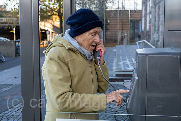 Deutschland, Bremen - Ruestige Rentnerin waehlt eine Nummer an einer Telefonzelle der Deutschen Telekom