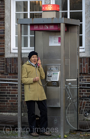Deutschland, Bremen - Ruestige Rentnerin telefoniert an einer Telefonzelle der Deutschen Telekom