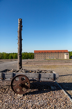 Deutschland, Weimar - Gedenkstaette Buchenwald (KZ-Gedenkstaette), Pfahl und Karren Symbole fuer Zwangsarebeit und Bestrafung, hinten Kammergebaeude (Haeftlingsbekleidungskammer), heute Museum