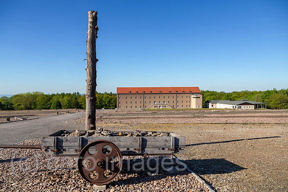 Deutschland, Weimar - Gedenkstaette Buchenwald (KZ-Gedenkstaette), Pfahl und Karren Symbole fuer Zwangsarebeit und Bestrafung, hinten Kammergebaeude (Haeftlingsbekleidungskammer), heute Museum