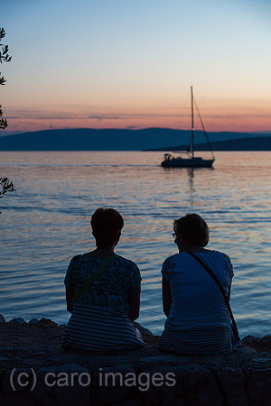 Kroatien, Krk (Hauptstadt der Insel Krk) - Zwei Frauen am Strand geniessen die Abenddaemmerung mit Blick auf die Bucht vor Krk
