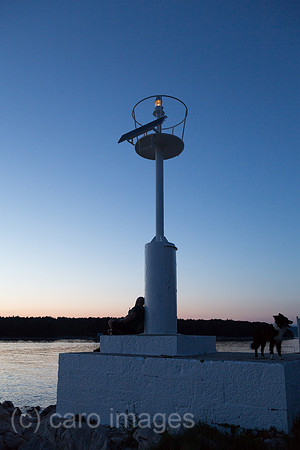 Kroatien, Krk (Hauptstadt der Insel Krk) - Mann mit Hund am Leuchtturm des Yachthafens geniesst die Abenddaemmerung