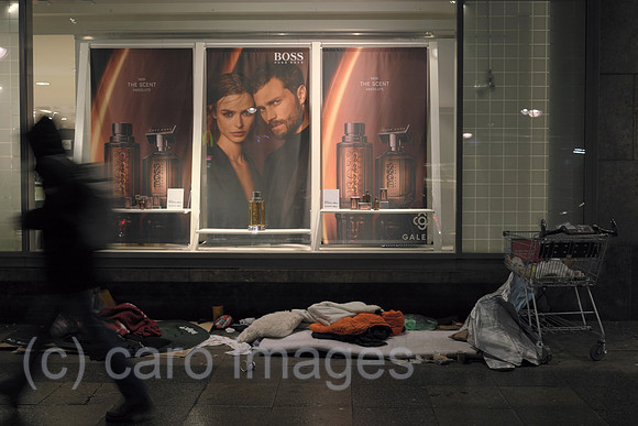 Deutschland, Berlin - Utensilien von Obdachlosen vor Schaufenster von Karstadt mit Werbefoto fuer Parfuem der Edelmarke Boss