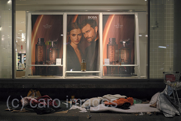 Deutschland, Berlin - Utensilien von Obdachlosen vor Schaufenster von Karstadt mit Werbefoto fuer Parfuem der Edelmarke Boss