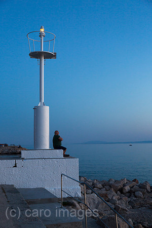 Kroatien, Krk (Hauptstadt der Insel Krk) - Mann am Leuchtturm des Yachthafens geniesst die Abenddaemmerung