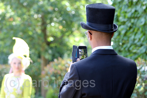 Royal Ascot, Grossbritannien, Mann mit Zylinder macht ein Foto von seiner Frau mit seinem Smartphone