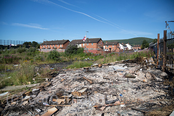 Grossbritannien, Nordirland, Belfast - Protestantischer Teil von West Belfast - verwahrloster, verbrannter Platz nach dem bonfire vom Orangemens Day, links der Peace Wall