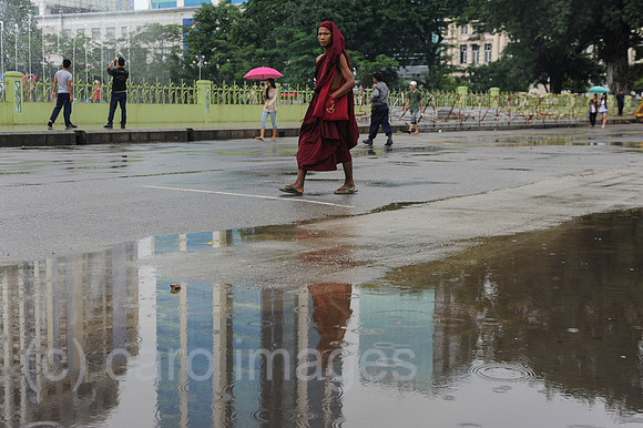 Yangon, Myanmar, Buddhistischer Moench geht in der Regenzeit eine Strasse entlang