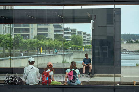 Schweiz, Opfikon - Passagiere warten an Tramhaltestelle, Peripherie von Zuerich, hinten das moderne Glattpark Wohnquartier