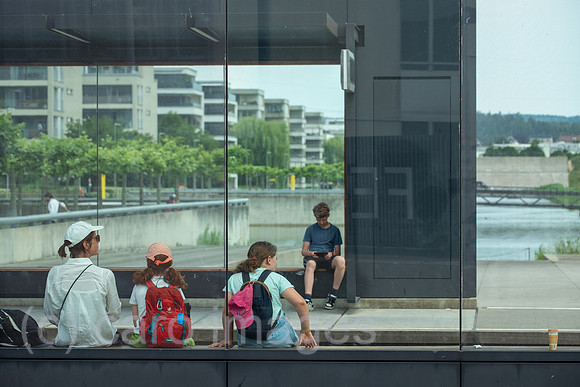 Schweiz, Opfikon - Passagiere warten an Tramhaltestelle, Peripherie von Zuerich, hinten das moderne Glattpark Wohnquartier