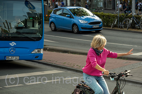 Deutschland, Muenster - Seniorin auf dem Fahrrad auf einer Hauptstrasse in der City