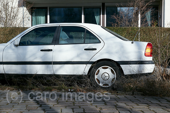 Berlin, Deutschland - Parkender weisse Mercedes Limousine am Strassenrand waechst allmaehlich mit Gras und Baumtrieben zu.