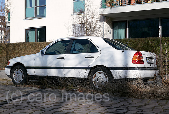 Berlin, Deutschland - Parkender weisse Mercedes Limousine am Strassenrand waechst allmaehlich mit Gras und Baumtrieben zu.