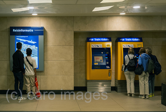 Netherlands, Amsterdam - passengers in front of ticket vending machines and a screen with travel information in Centraal Station (central station)