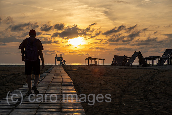 Albanien, Divjaka - Befestigter Weg fuer Fussgaenger ueber den Strand zum Meer an der Adriakueste im Nationalpark Divjaka-Karavasta, rechts Daecher fuer Sonnenschutz und Liegen